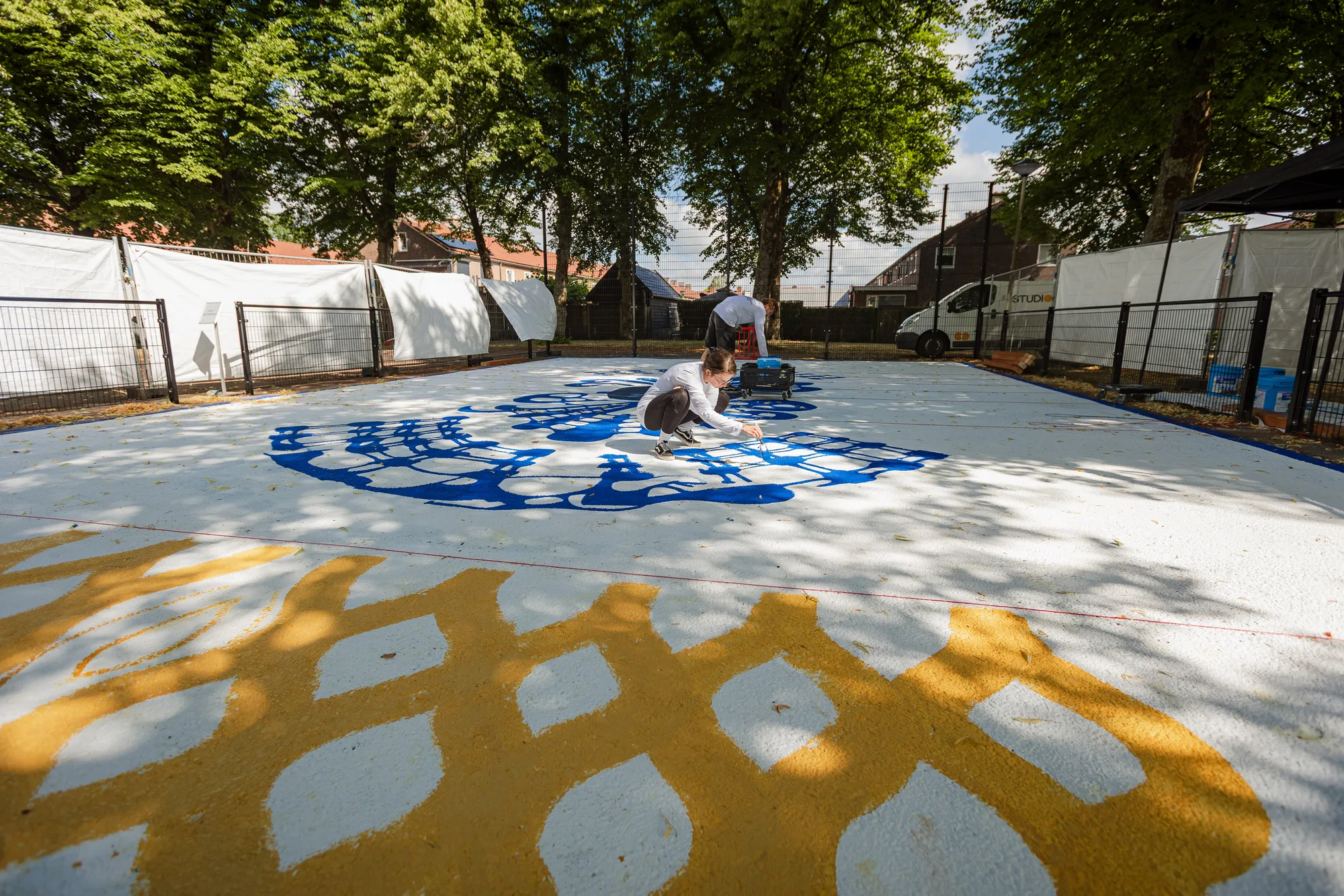 Basketbalveldje aan de Wattstraat met een vloerschildering van een kobaltblauw tapijtpatroon, schilders aan het werk