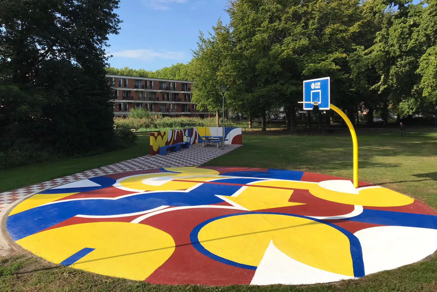 Basketbalveld in het Brabantpark met een vloerschildering van grote cirkels in rood, geel en kobaltblauw, met een gele basketbalpaal