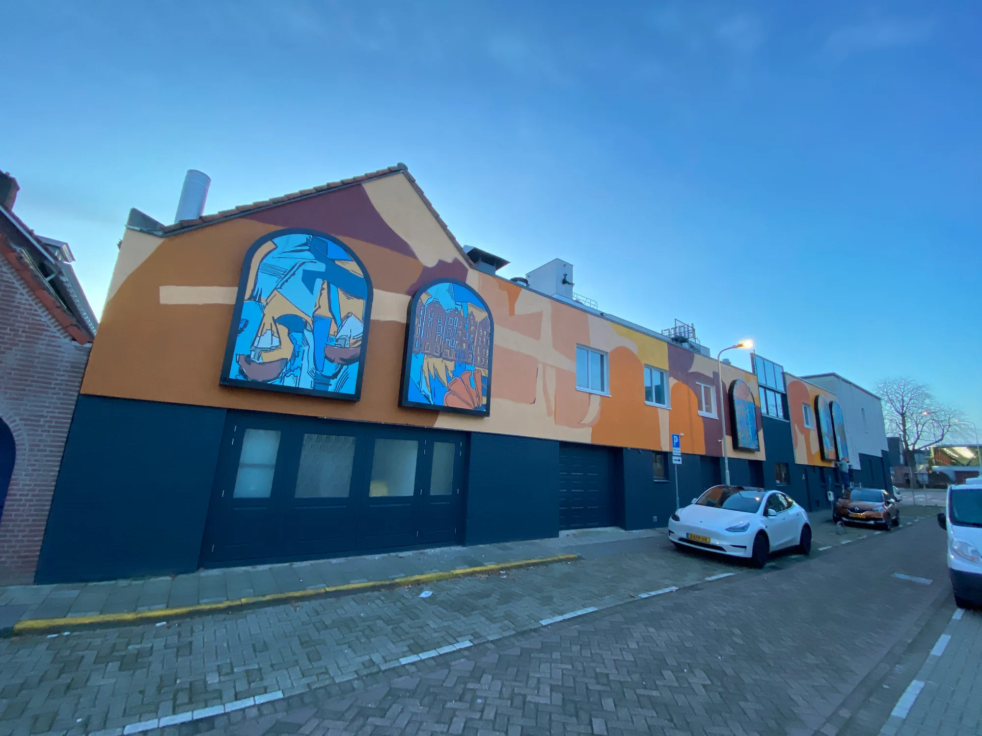 Gevel van een woning in Roosendaal met twee verlichte lichtbakken met schilderingen, onder een strakblauwe lucht