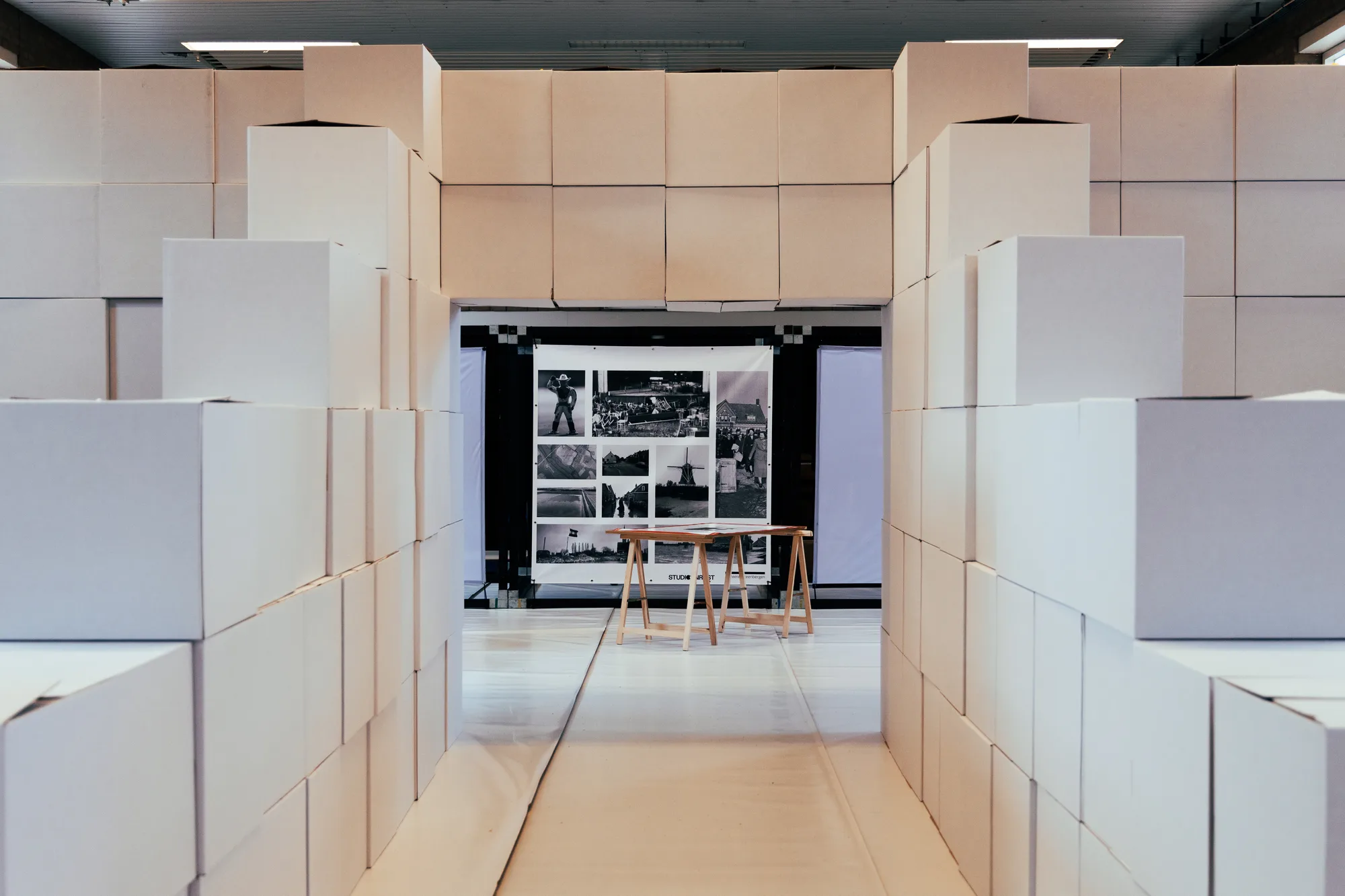 Levensgrote maquette van de fietstunnel uit witte dozen in de gymzaal van Nieuw-Vossemeer, met aan het eind een tafel met foto’s