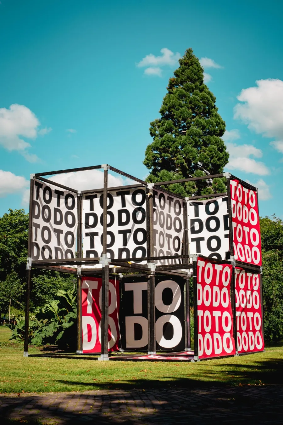 Het kunstobject TO DO, een kubus van rode en zwarte panelen met de letters TO DO, in een park in Roosendaal