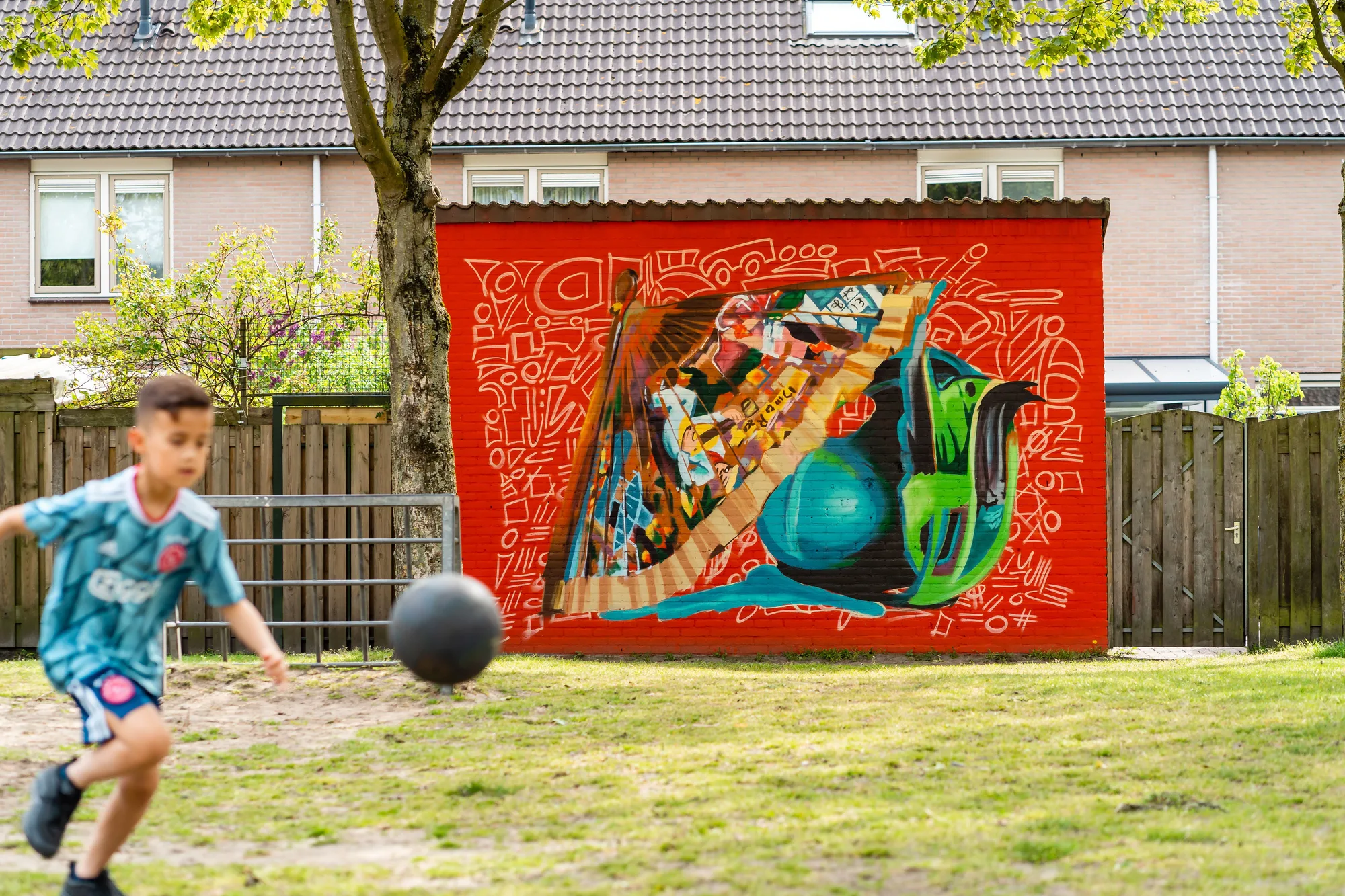 Jongen speelt met een bal voor een rode muurschildering met een groene bal en een kinderboek in de wijk Het Blauwe Roodborstje
